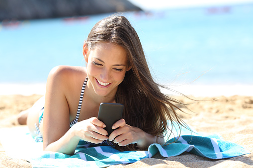 Happy girl in bikini using smart phone on the beach