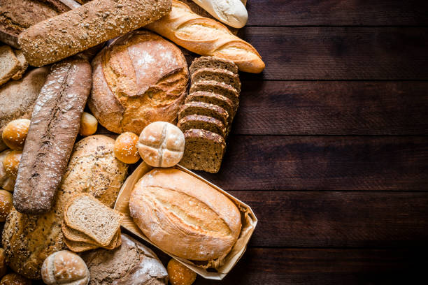 Breads assortment with copy space on rustic wooden table Top view of breads assortment like brunch bread, rolls, wheat bread, rye bread, sliced bread, wholemeal toast, spelt bread and kamut bread on dark brown rustic wooden table. Breads are at the left side of the image leaving a useful copy space at the right side on the table. Low key DSLR photo taken with Canon EOS 6D Mark II and Canon EF 24-105 mm f/4L bread stock pictures, royalty-free photos & images