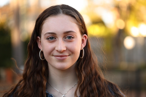 Close up of smiling redhead teen girl looking at camera standing in summer park. Close up of pretty happy teenage kid smiling at camera outdoors