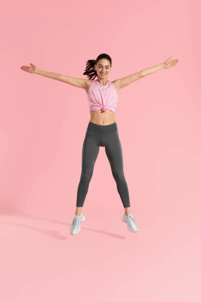 istock Fitness jump. Woman doing jumping exercise on pink background 1163715478