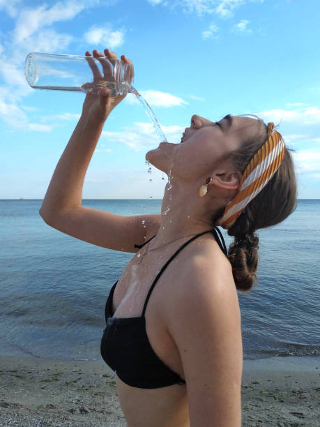 Unrecognizable woman opening a plastic bottle of water, enjoying a refreshing drink in a warm, sunny environment
