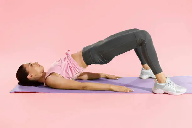Photo of Fitness woman doing hip workout exercise on yoga mat at studio