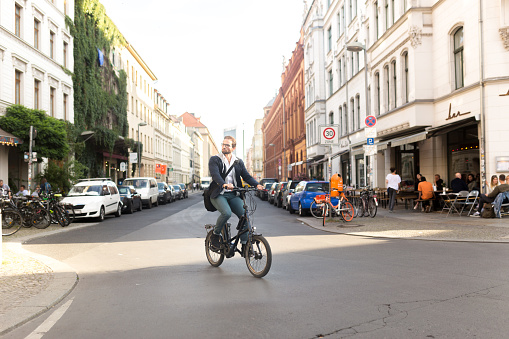 Photo series of a young adult male commuting with electric bicycle through Berlin and doing business at the same time, drinking coffee from reusable coffee cup, listening to podcasts and making business calls.