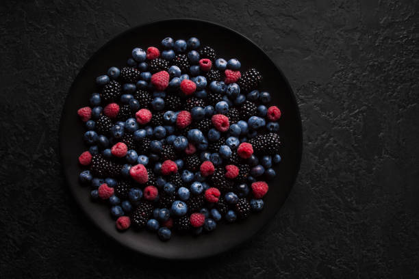 istock Different blueberries, raspberries and blackberries on a black plate and a dark background. Close-up shot from the top. 1163724707