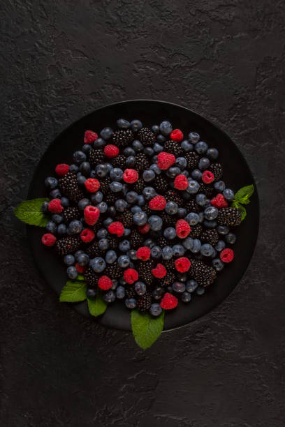 istock Different blueberries, raspberries and blackberries on a black plate and a dark background. Close-up shot from the top. 1163724719