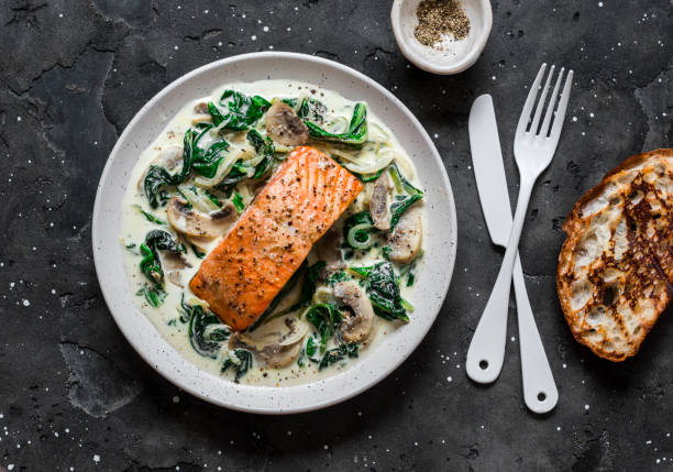 Baked salmon with creamy spinach mushrooms sauce on a dark background, top view. Salmon florentine Baked salmon with creamy spinach mushrooms sauce on a dark background, top view. Salmon florentine salmon seafood stock pictures, royalty-free photos & images