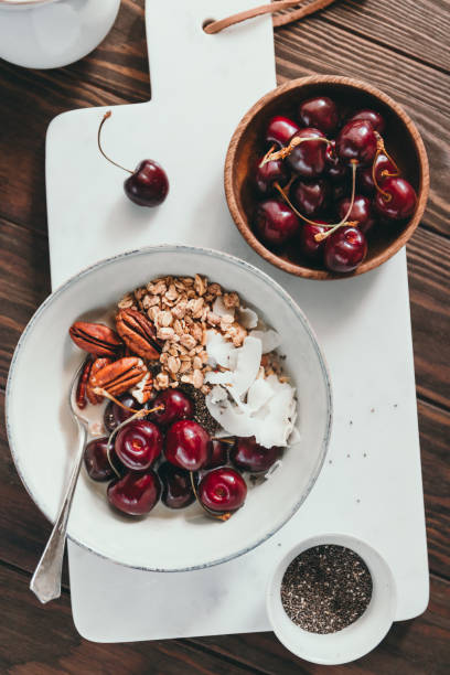 Healthy summer vegetarian breakfast with granola, cherry, pecans, coconut flakes, chia and oat milk on marble tray.