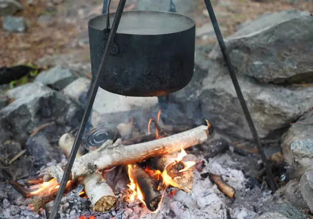 Cooking herbal tea with open fire. Burning firewood and smoke. Halt and rest on walking path.