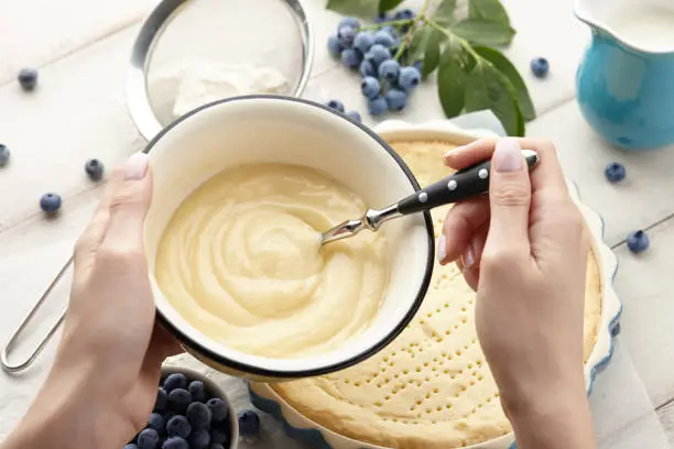 Woman preparing whipped cream for blueberry pie with fresh berries. Blueberry tart cooking recipe.