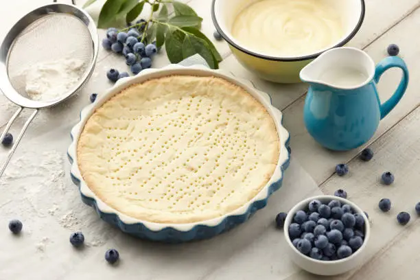 Pie crust, custard and fresh blueberries on white wooden planks. Cooking blueberry pie.