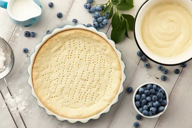 Pie crust, custard and fresh blueberries on white wooden planks. Cooking blueberry pie.