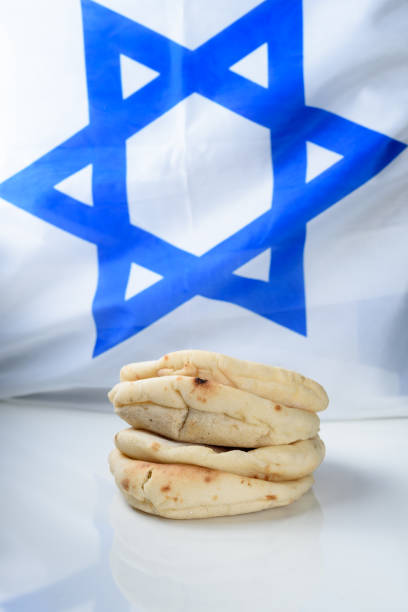 istock Stack freshly baked pittas on wooden board over israel flag background. 1163733750