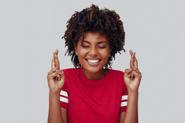 Attractive young African woman Attractive young African woman keeping fingers crossed and smiling while standing against grey background fingers crossed stock pictures, royalty-free photos & images