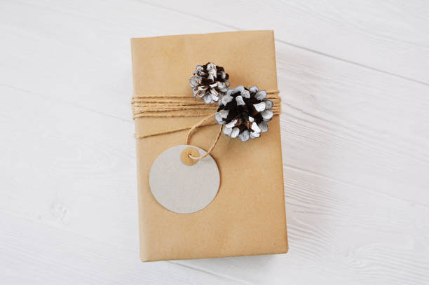 istock Kraft Christmas gift box with rope, mockup tag, cones on white background. Close up top view 1163739888