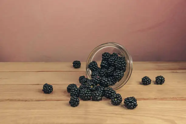 Fresh blackberry in glass bowl on a brown wooden table and dark-red wall background.