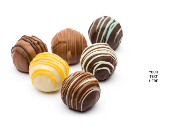 Six delicious luxury Chocolate truffles on bed of milk, white and dark chocolate balls. Presented on a classic square white plate with cocoa dusted background.