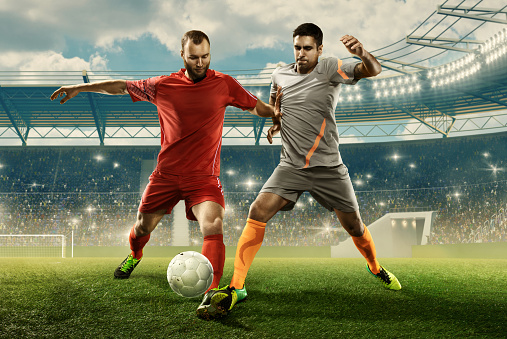 Two professinal soccer players in sports uniform  fight for a ball on a stadium
