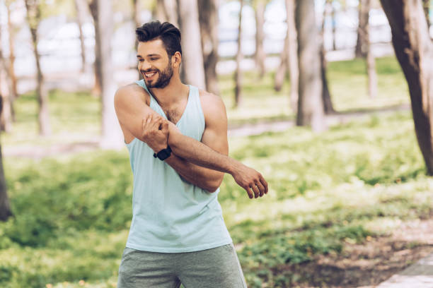 istock cheerful young sportsman smiling while stretching in sunny park 1163755348