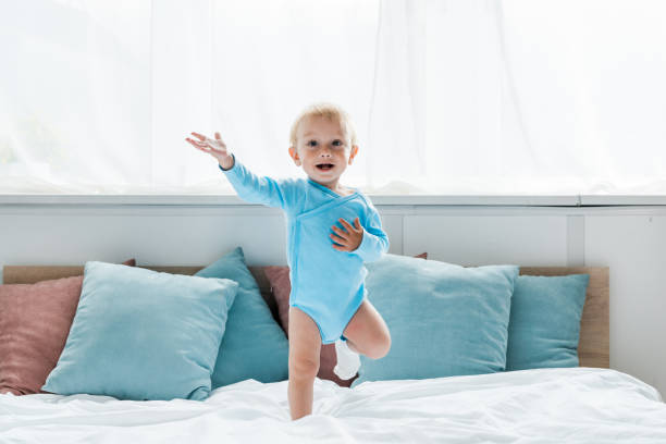 istock cheerful kid gesturing while jumping on bed in modern bedroom 1163756139