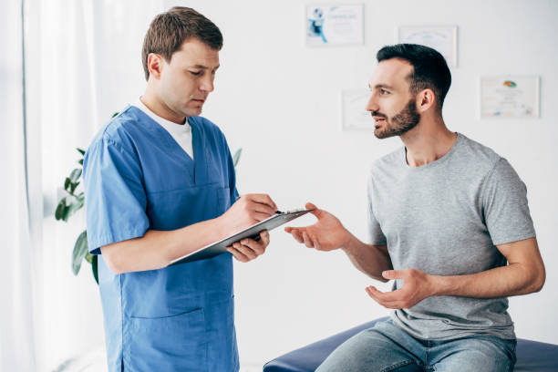 patient s'asseyant sur le divan et le docteur écrivant la prescription dans le cabinet de massage à la clinique - male doctor photos et images de collection