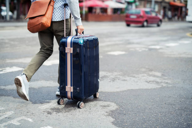 istock Traveler man walking with rolling suitcase in pedestrian crossing 1163758130