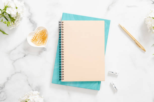 istock Modern home office desk workspace with blank paper notebook, white flowers and feminine accessories on marble background. Flat lay, top view, overhead. Woman workspace concept. 1163764098