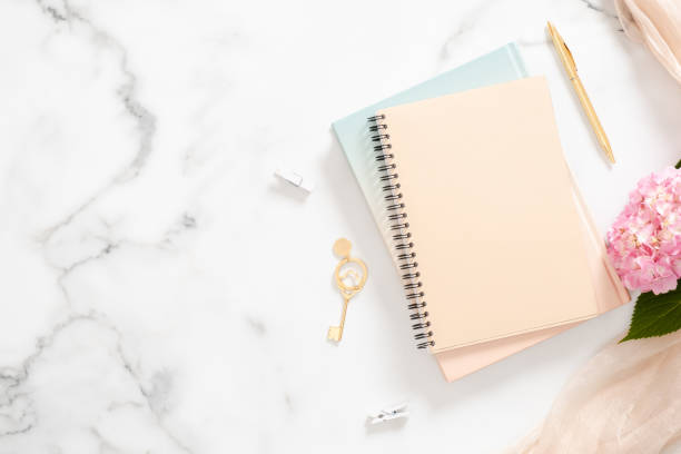 istock Modern home office desk workplace with blank paper notebook, pink hydrangea flower, pastel blanket and golden accessories on marble background. Beauty blogger workspace concept. Flatlay, top view. 1163764106