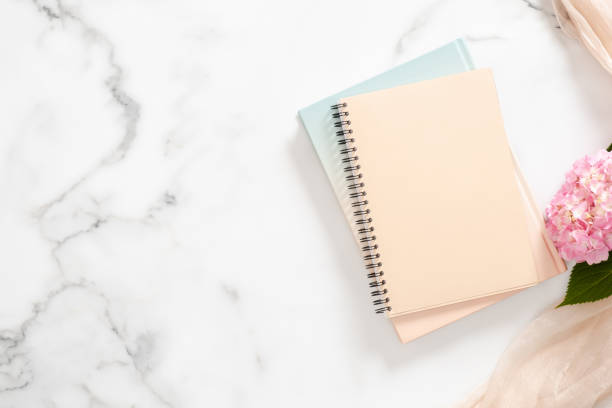istock Blank paper notebook, pink hydrangea flower, pastel blanket on marble background. Flat lay, top view home office desk. 1163764108