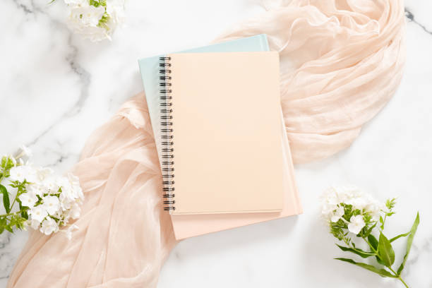 istock Blank paper notebook, white flowers, pastel blanket on marble background. Flat lay, top view home office desk. Beauty blogger workspace concept. 1163764132
