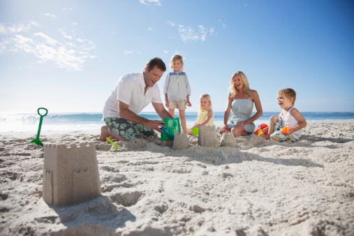 Happy family with little kids enjoying time at the sea in exotic country,building sand castle.