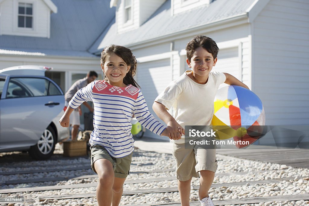 Hermano y hermana con una pelota de playa corriendo en la entrada - Foto de stock de Coche libre de derechos