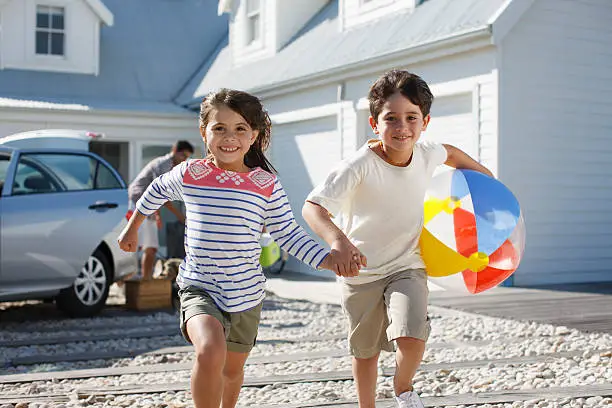 Photo of Brother and sister with beach ball running on driveway