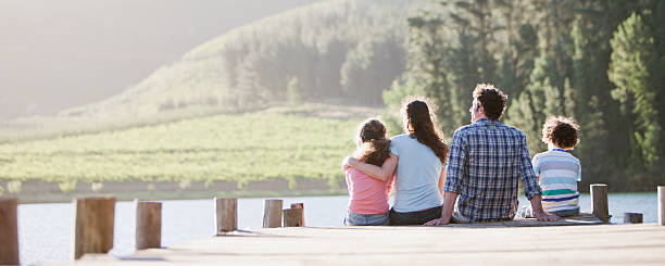 famiglia seduto sul dock dal lago - mother lifestyles father horizontal foto e immagini stock