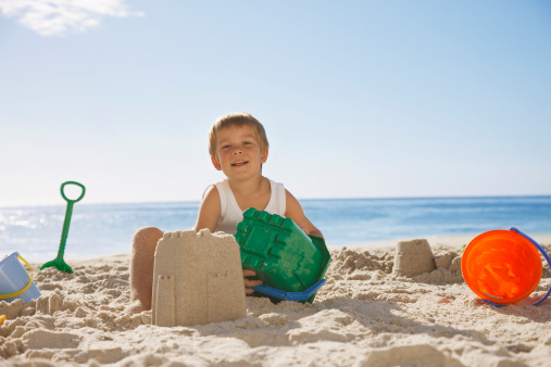 happy little boy with built sandcastle on tropical beach