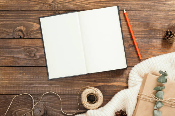 istock Autumn flatlay composition. Top view on book with empty pages, red pen, rope, gift box on wooden background. Autumn hygge style desk table or winter holiday concept. 1163770648