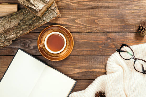 istock Hygge style flatlay composition with cup of tea, book with empty pages, white knitted scarf, woman glasses, firewood on wooden desk table. Autumn or winter holidays concept. Flat lay, top view. 1163770650