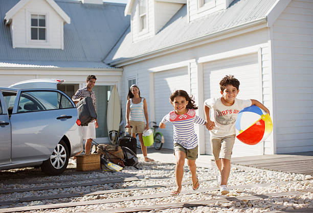 brother and sister with beach ball running on driveway - baggage fotos stockfoto's en -beelden