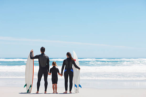 familie in neoprenanzüge, surfbretter hände halten am strand - bonding horizontal surfing surf stock-fotos und bilder