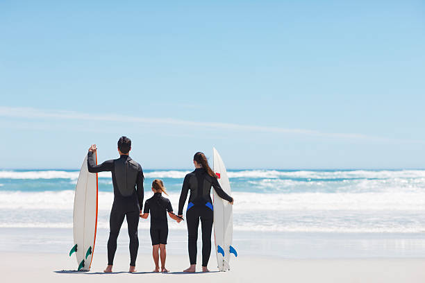 Family in wetsuits with surfboards holding hands on beach  wetsuit stock pictures, royalty-free photos & images