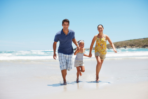 Parents with their child sitting in the sand on the seashore in sunny day. Concept of the family vacation and tourism.