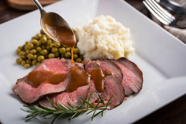 vertiendo salsa de salsa en rodajas de carne asada con patata sorda y guisantes dulces - roast beef fotografías e imágenes de stock