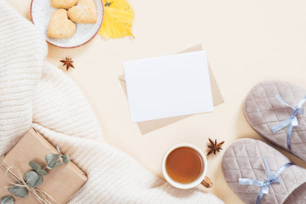 istock Autumn flatlay composition. Feminine desktop with white knitted plaid, letter, gift box, slippers, tea cup, fallen leaves on pastel beige background. Flat lay, top view. Autumn, fall concept. 1163771690