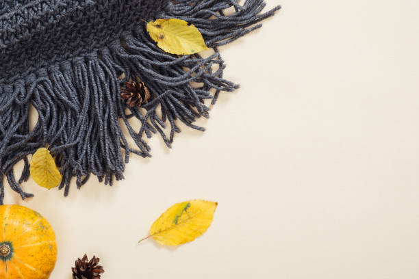 Autumn composition. Flatlay knitted scarf, fallen leaves, pumpkin, cone on pastel beige background. Flat lay, top view, copy space. Autumn fall and thanksgiving concept.