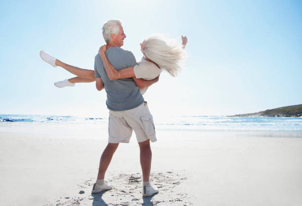 mann spinning frau am strand - couple senior adult travel action stock-fotos und bilder