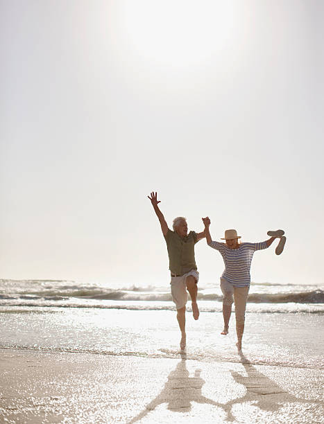 sênior casal pulando na praia - couple senior adult travel action - fotografias e filmes do acervo