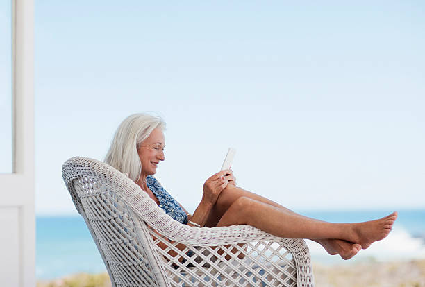 mujer senior usando tableta digital en silla - summer people furniture vacations fotografías e imágenes de stock