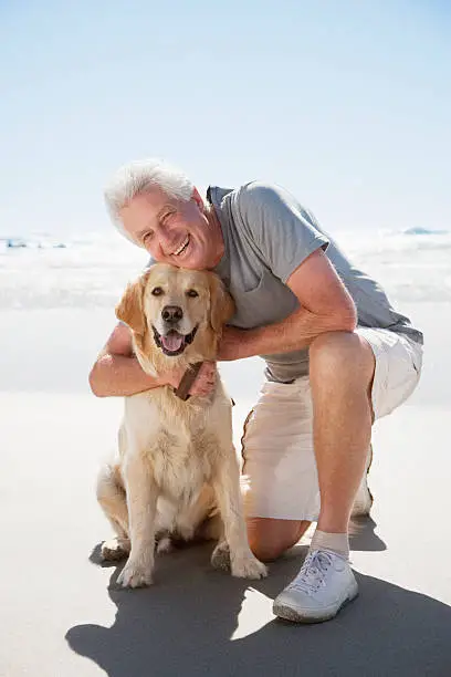 Photo of Senior man hugging dog on beach