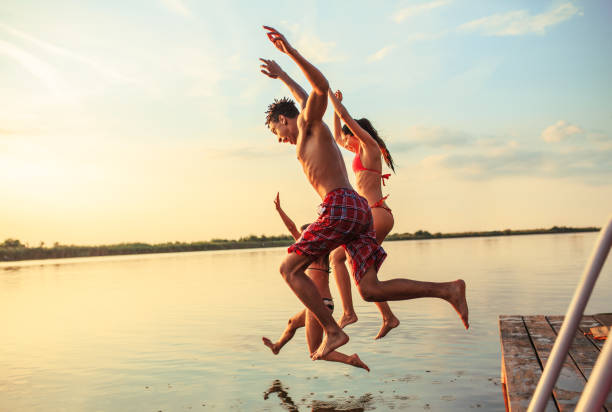 Summer day fun. Group of friends jumping into the lake from wooden pier. Summer day fun. jumping into water stock pictures, royalty-free photos & images
