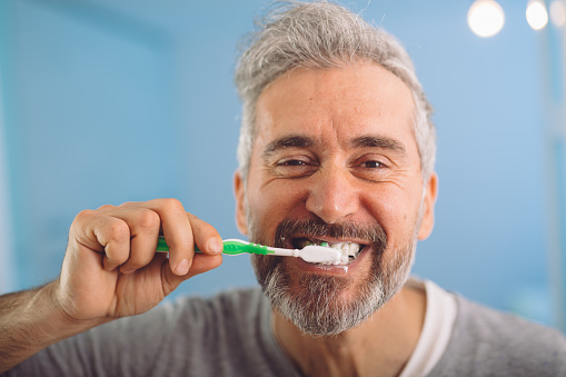 happy middle aged gray haired bearded man brushing his teeth