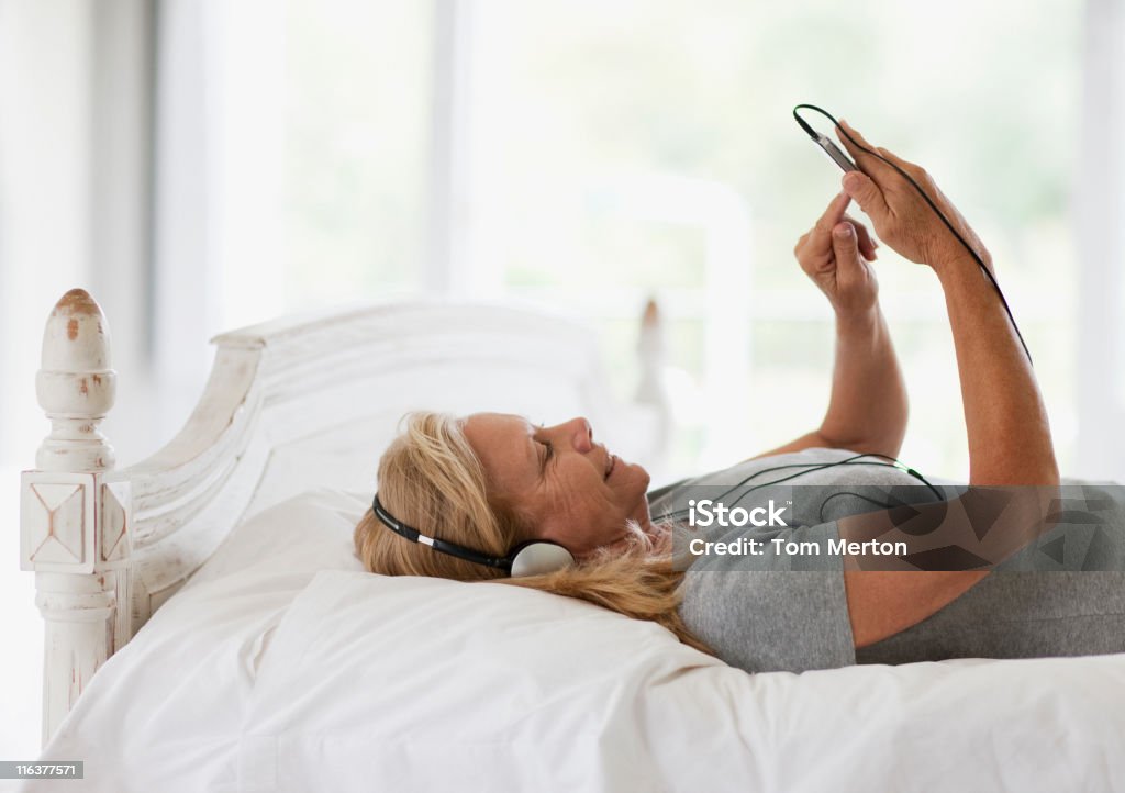 Donna posa sul letto e ascoltare musica sul lettore mp3 - Foto stock royalty-free di Letto